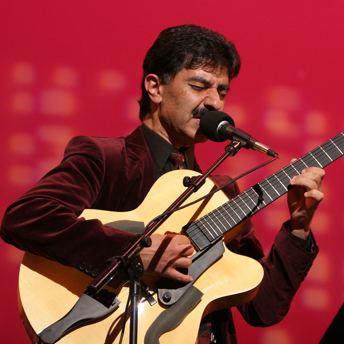 Musician John Baboian sings into a microphone while accompanying himself on the guitar