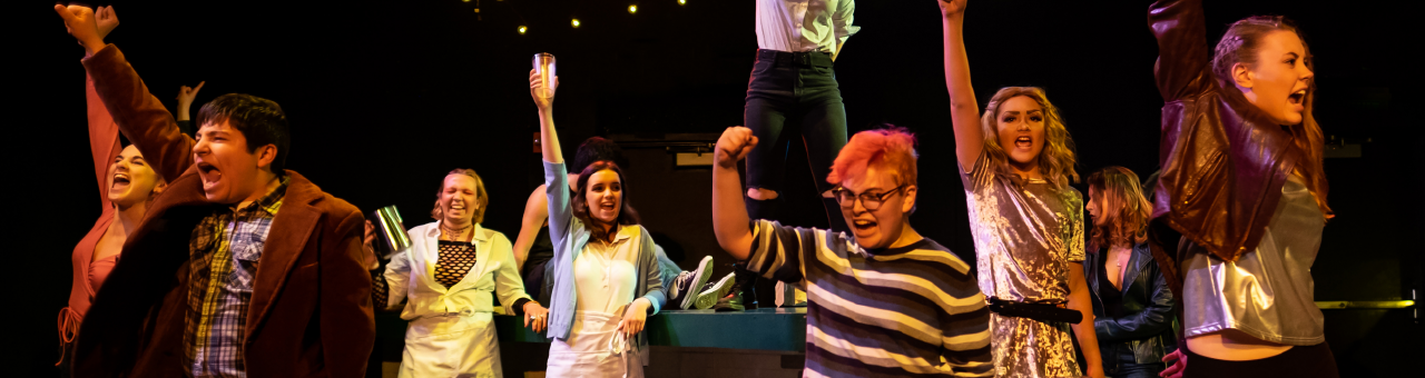 Actors from WCT's Rent with fists raised triumphantly in the air