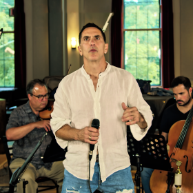 Vocalist Steven Santoro with mic in hand performing in front of a violinist and cellist